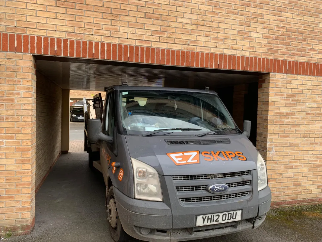 An EZSKIPS lorry driving through a narrow archway under a brick building