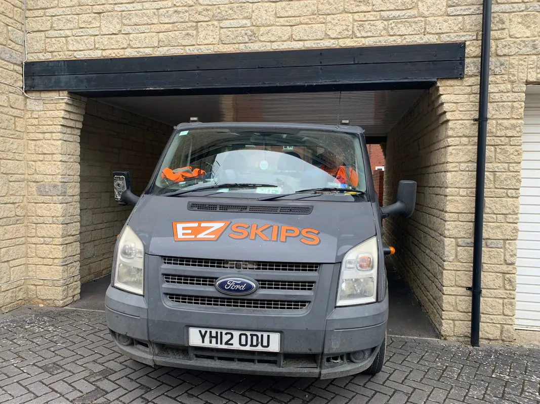 An EZSKIPS lorry parked under a stone carport