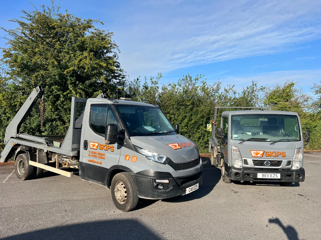 Two EZSKIPS lorries in a yard, one with its skip arms raised