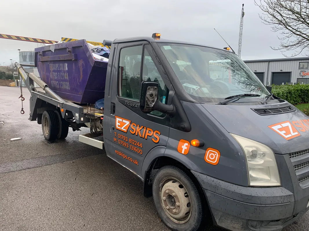 An EZSKIPS lorry in the orange and grey livery, carrying a purple skip