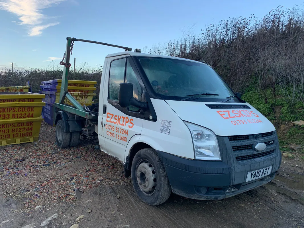 A white EZSKIPS skip lorry beside a row of yellow skips